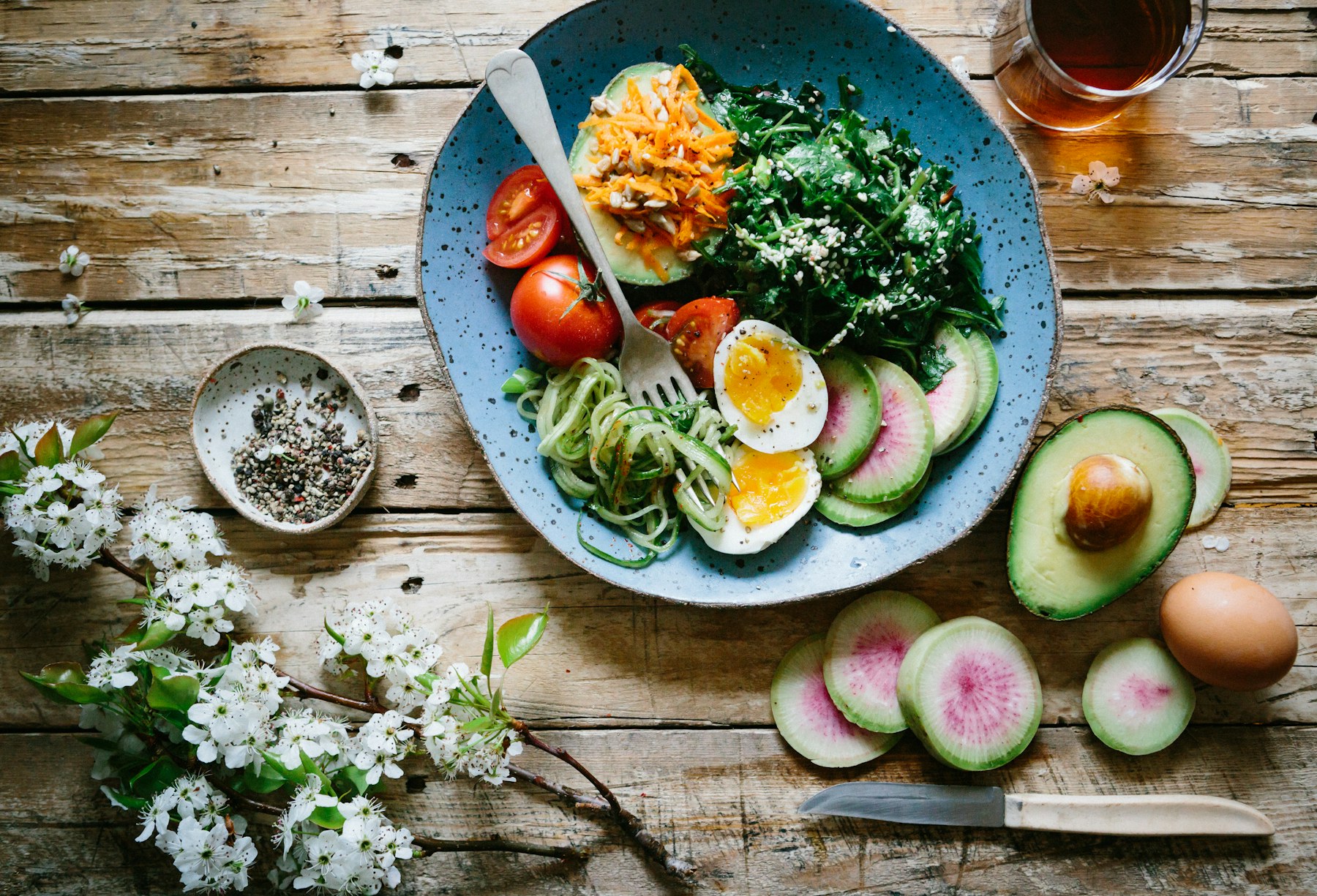 Healthy bowl with eggs, greens, avocado and vegetables on a rustic table