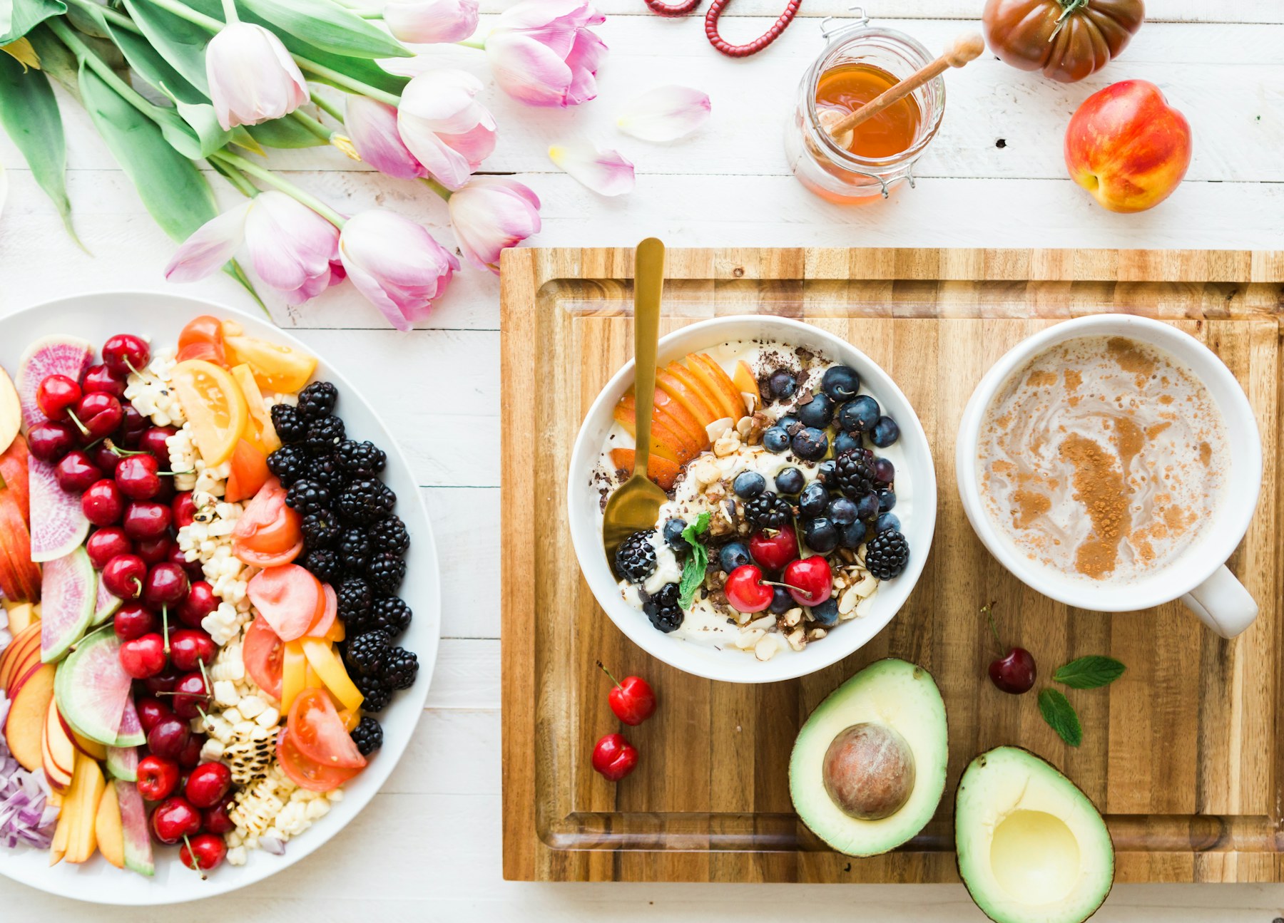 Bright breakfast table with fruit, oat bowl, coffee, avocado and tulips