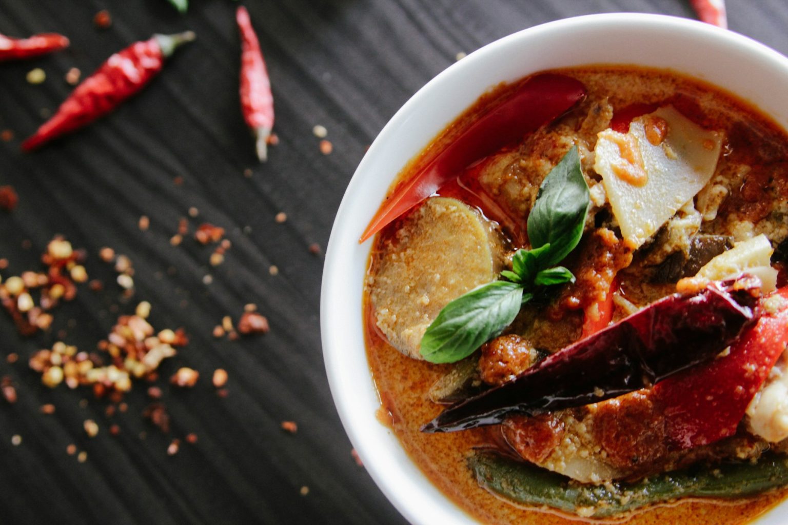 Rich red stew in a white bowl with herbs and chili