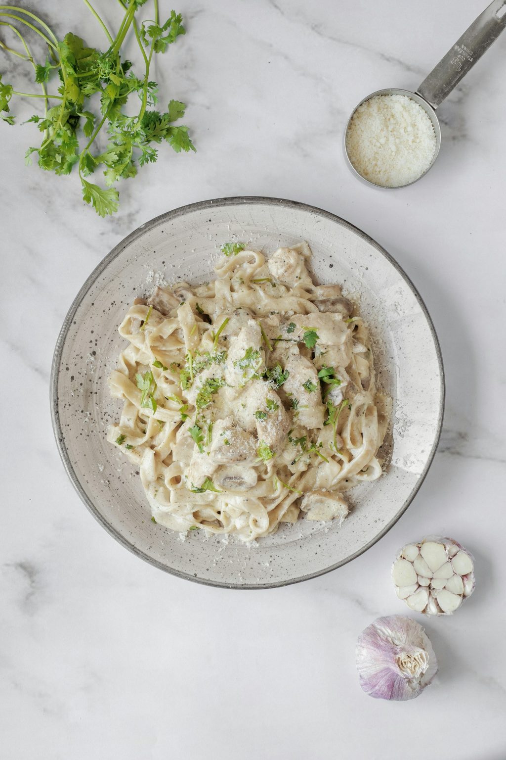 Creamy high-protein chicken pasta with Parmesan and fresh herbs in a speckled bowl, with garlic and grated cheese on marble