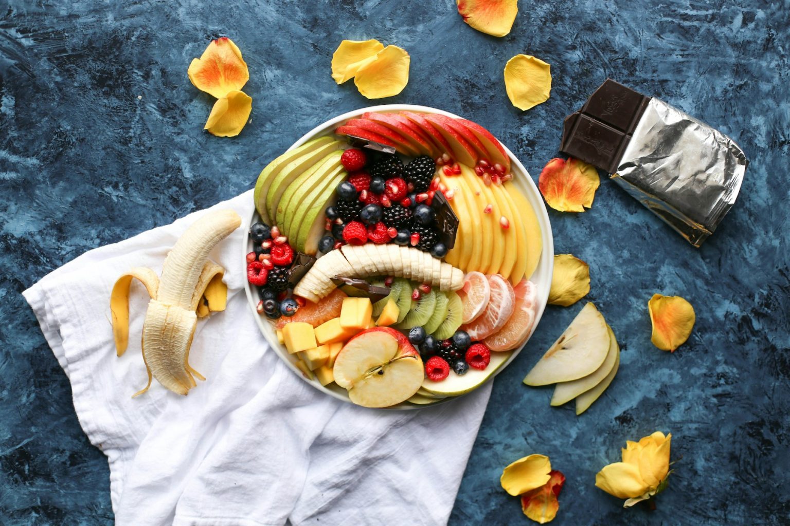 Fruit bowl with banana, berries and dark chocolate on a blue table